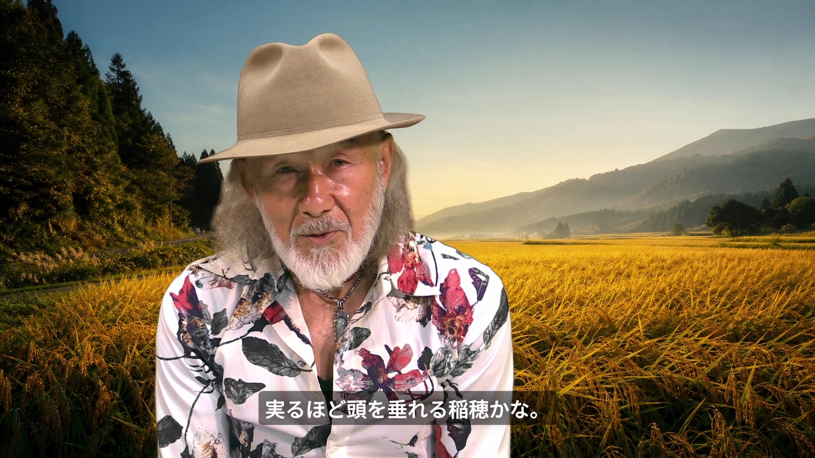 実った稲穂を背景に「実るほど頭を垂れる稲穂かな」と語るアーサー・ホーランド