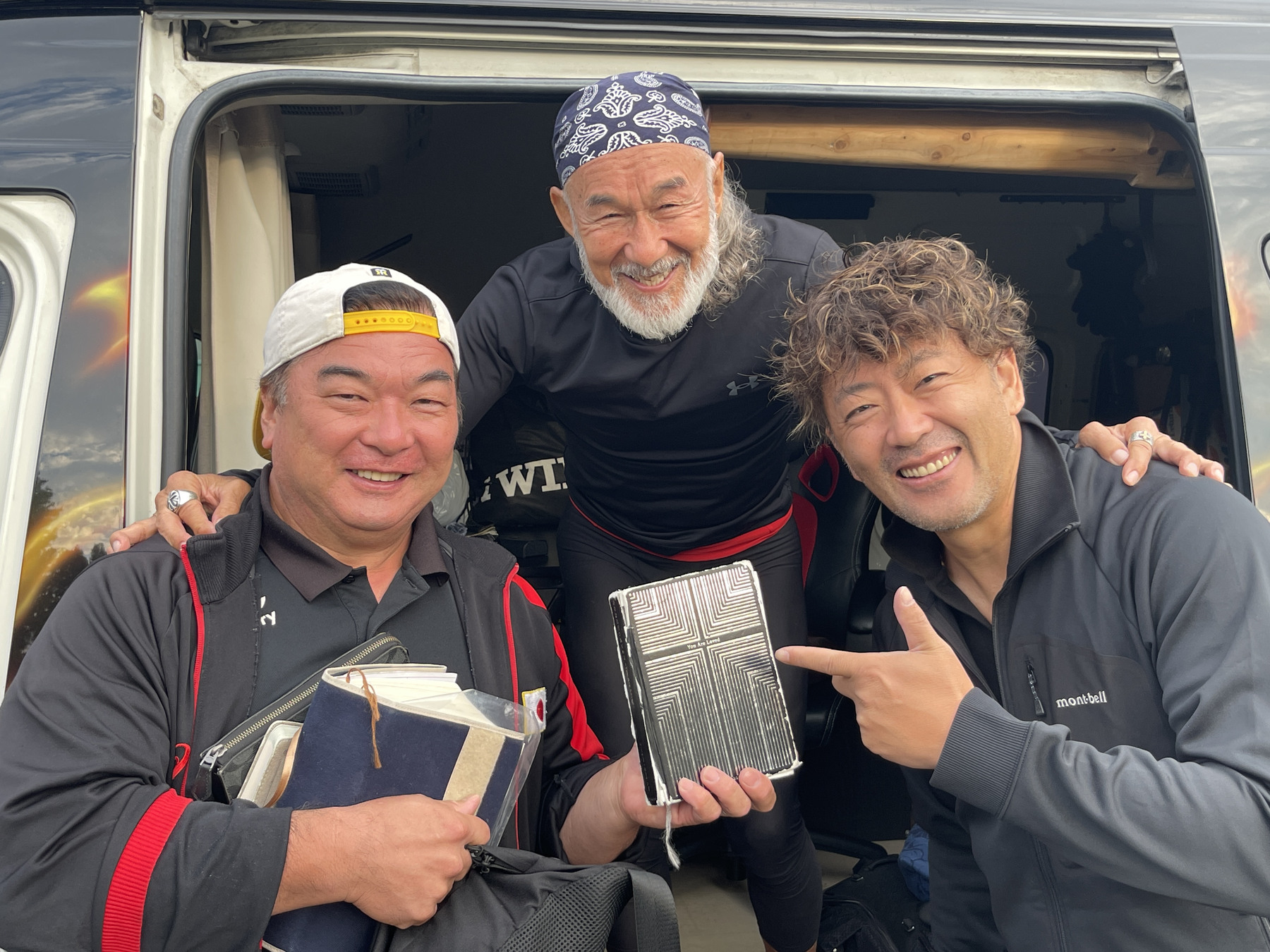 本を手に車のそばで並ぶアーサー先生と同行者