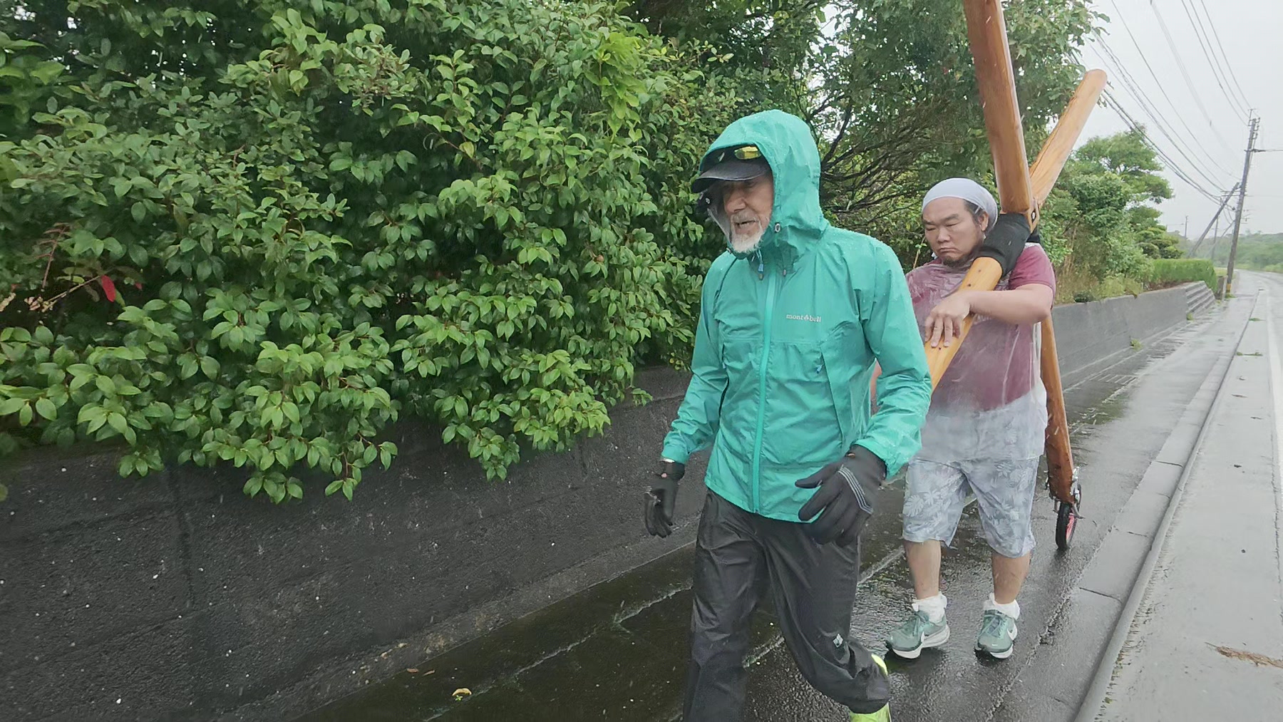 雨の道路脇を十字架を担いで進むアーサー先生と参加者