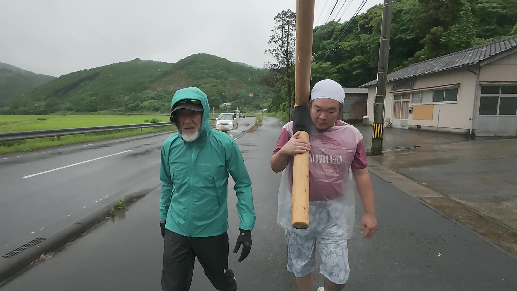 雨の道でアーサー先生と参加者が十字架を担いで歩く