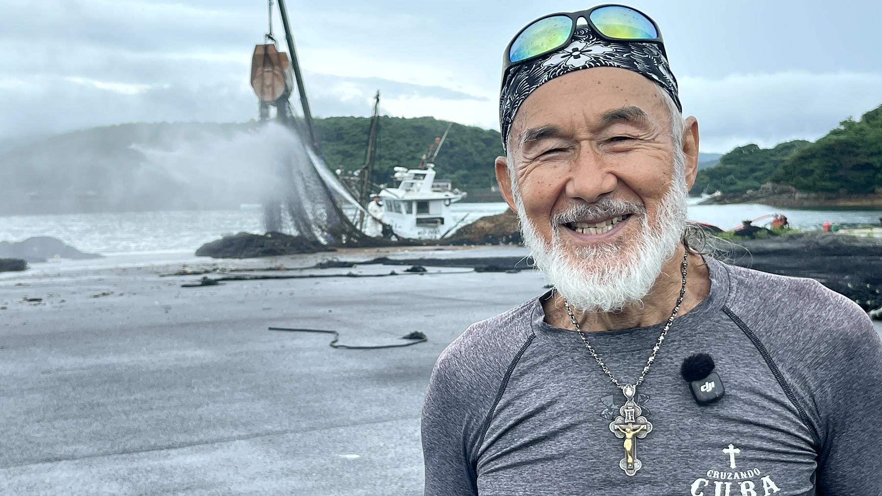 ゴール地点の海辺で網を洗う船を背に笑顔を見せるアーサー先生