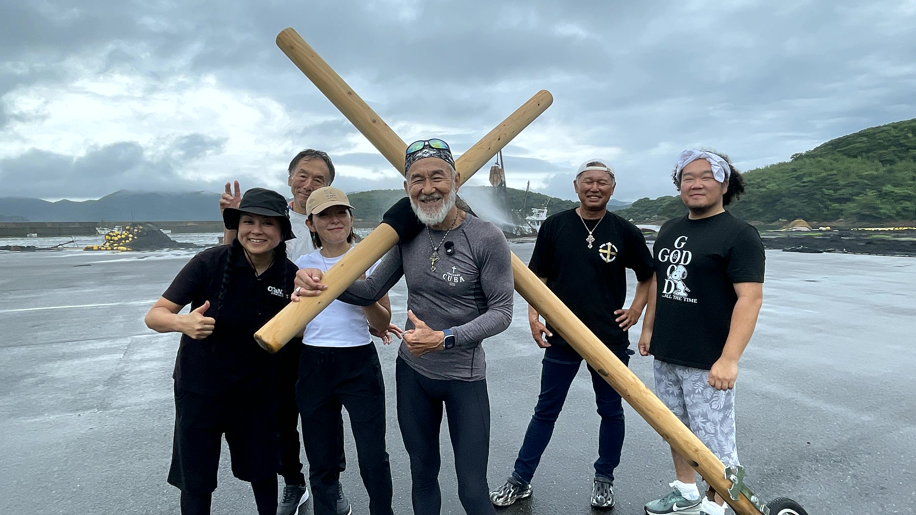 ゴール地点の海辺で十字架とともに立つアーサー先生と参加者たち