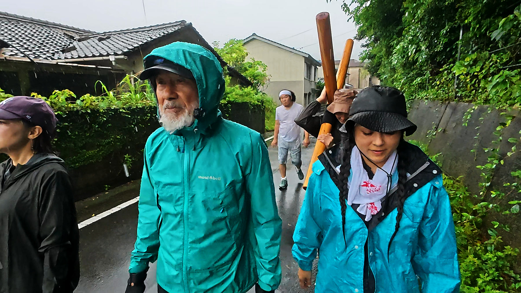奈留島の集落の道を十字架とともに歩くアーサー先生と参加者たち