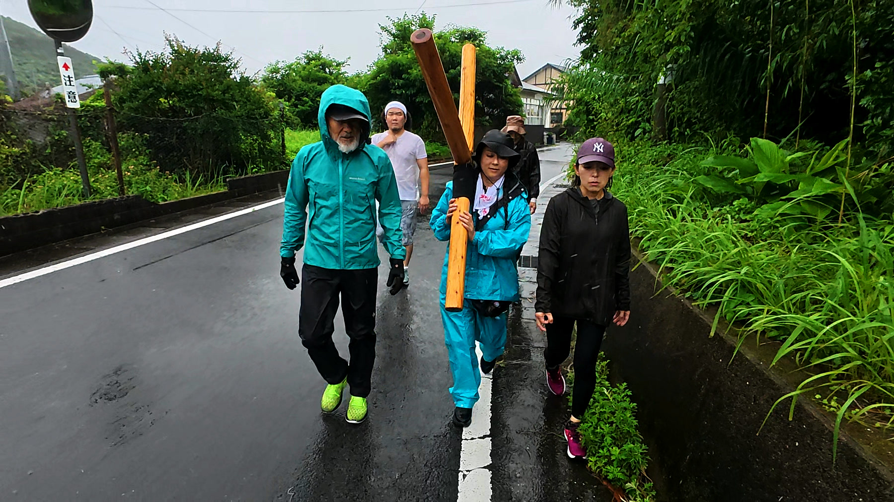 五島列島十字架行進4日目、奈留島の雨の道を十字架とともに歩くアーサー先生と参加者たち