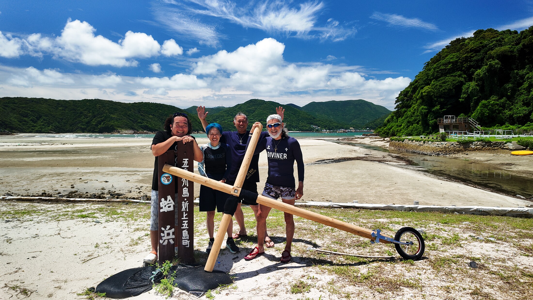 蛤浜の白い砂浜と青空の前で十字架とともに立つアーサー先生たち